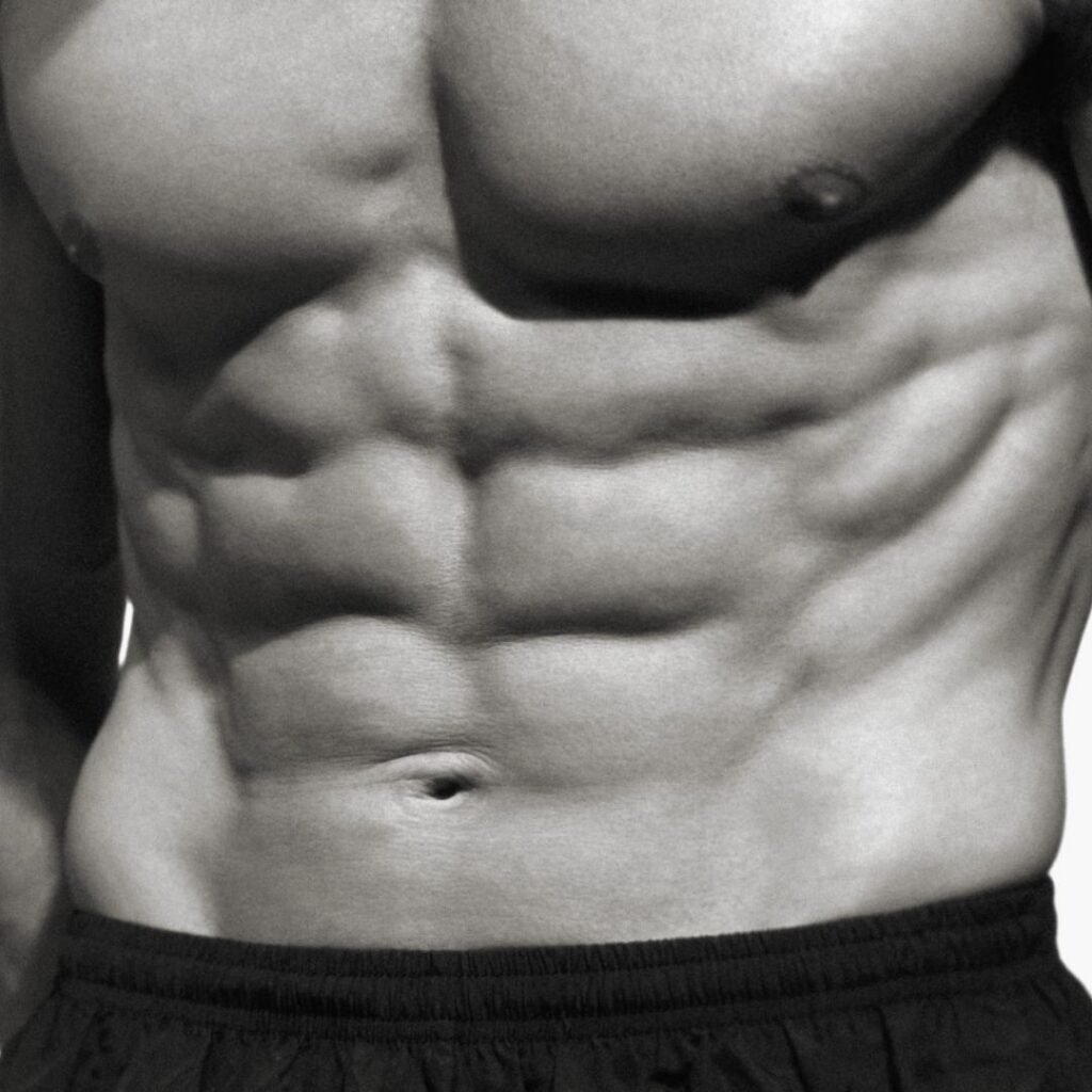 Detailed black and white close-up of a surgically sculpted male abdominal six-pack, representing liposuction results at Transform Head to Toe